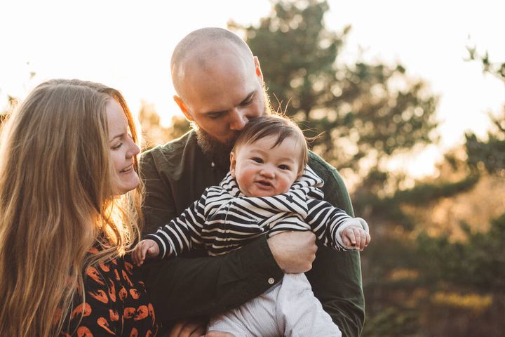 Familj med två föräldrar och en bebis utomhus en solig dag.