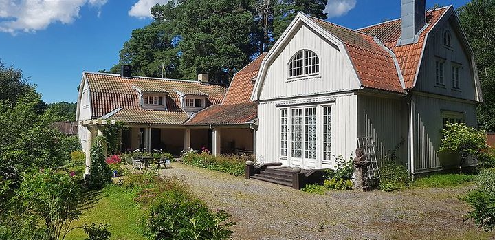 En vit villa med gula och röda tak, omgiven av grön trädgård, under en blå himmel.