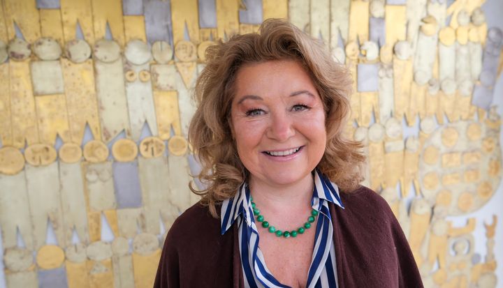 En kvinna står framför en stenmural. På väggen finns mönster av människor som står axel mot axel.