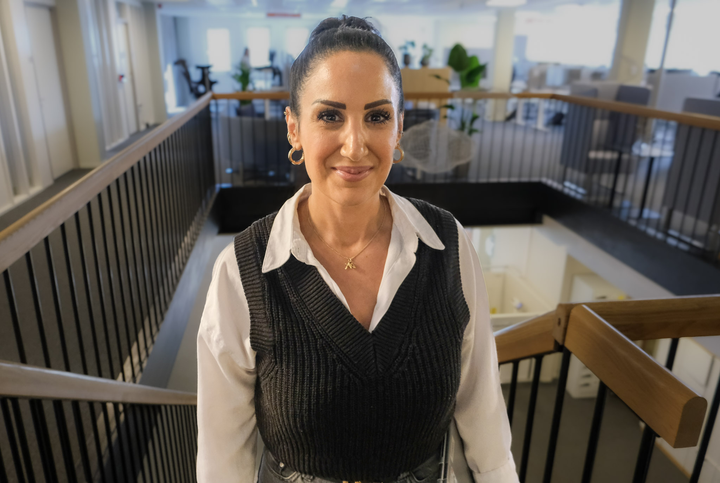 En person står i en trappa på ett kontor och ler mot kameran.