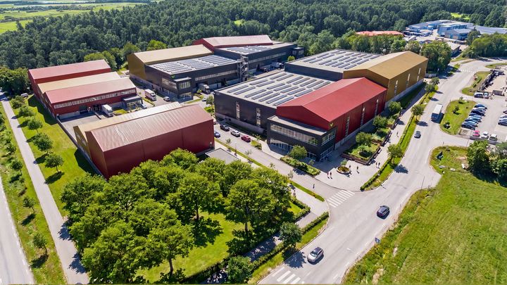 Flygbild av ett industriområde med flera stora byggnader omgivna av vägar och grönska.