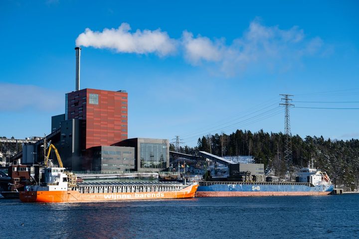 Bild av Igelsta kraftvärmeverk med en rökig skorsten och fartyg i hamnen.