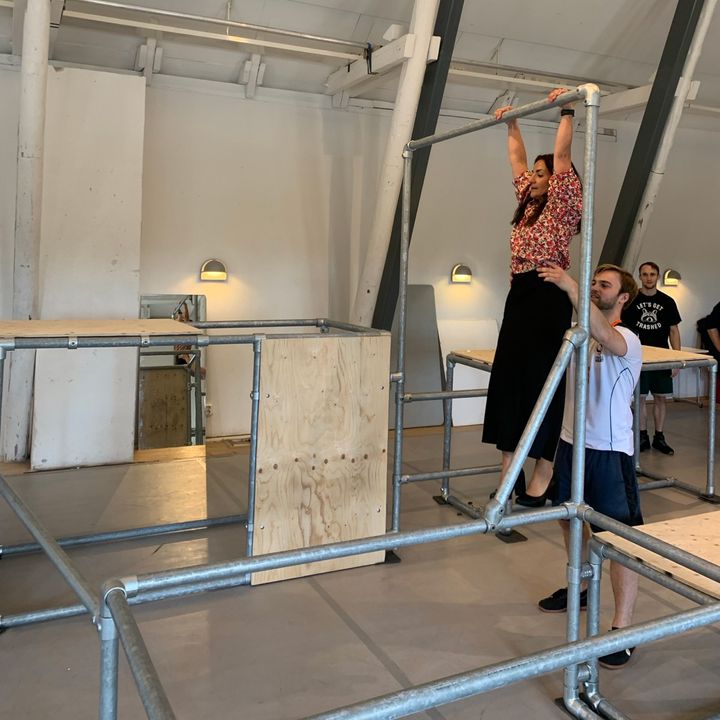 En person hänger från en ställning i en inomhussal med flera personer runt omkring.