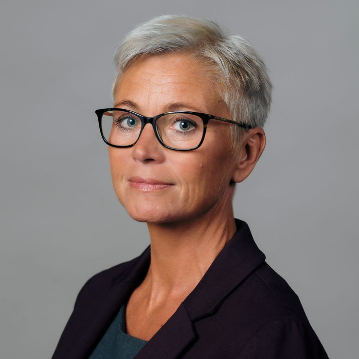 Kvinna med kort grått hår och glasögon, klädd i en mörk kavaj.