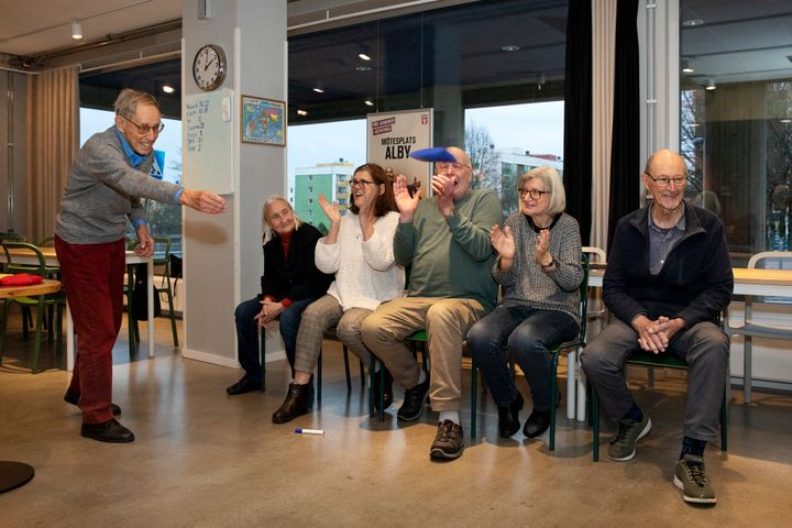 En grupp seniorer som deltar i en aktivitet där en person kastar en sandsäck medan de övriga klappar.