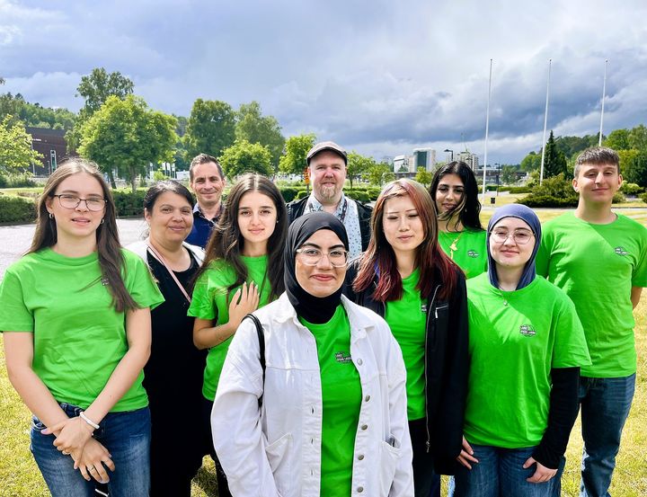 En grupp ungdomar i gröna tröjor står utomhus på en gräsmatta.