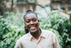 Kvinna står utomhus framför grönska och ler mot kameran.