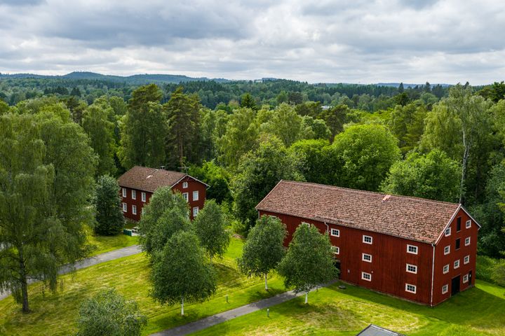 Fristad folkhögskola, två röda skolbyggnader omgivna av skog och växtlighet, fotat ovanifrån