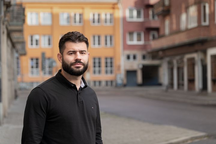 En man står på en gata framför byggnader.