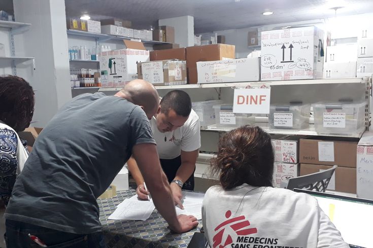 Fyra ur Läkare Utan Gränsers personal står kring ett bord och tittar på dokument, omkring dem är hyllor med medicinsk utrustning.