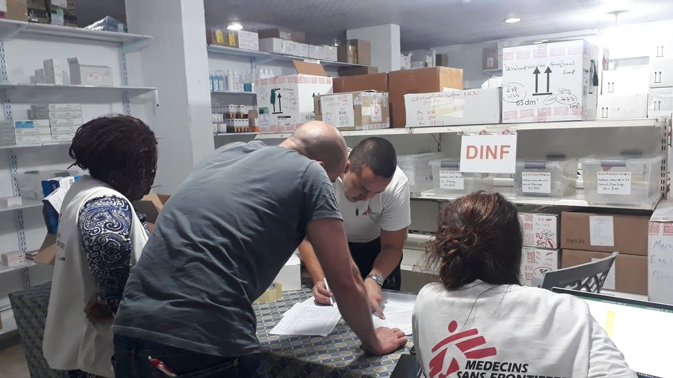 Fyra ur Läkare Utan Gränsers personal står kring ett bord och tittar på dokument, omkring dem är hyllor med medicinsk utrustning.