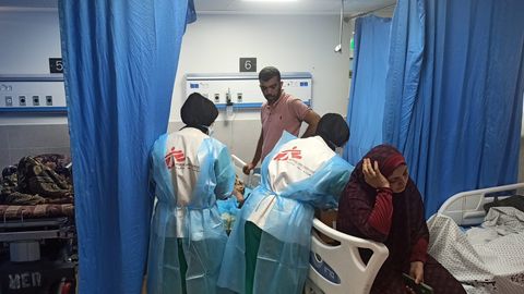 Två medarbetare på al Shifa-sjukhuset i Gaza står böjd över en person som ligger i en sjukhussäng. Bredvid sitter i kvinna på en annan säng.