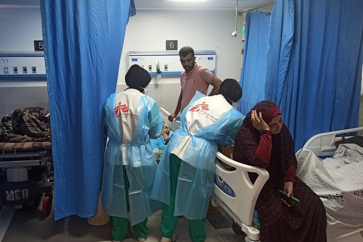 Två medarbetare på al Shifa-sjukhuset i Gaza står böjd över en person som ligger i en sjukhussäng. Bredvid sitter i kvinna på en annan säng.