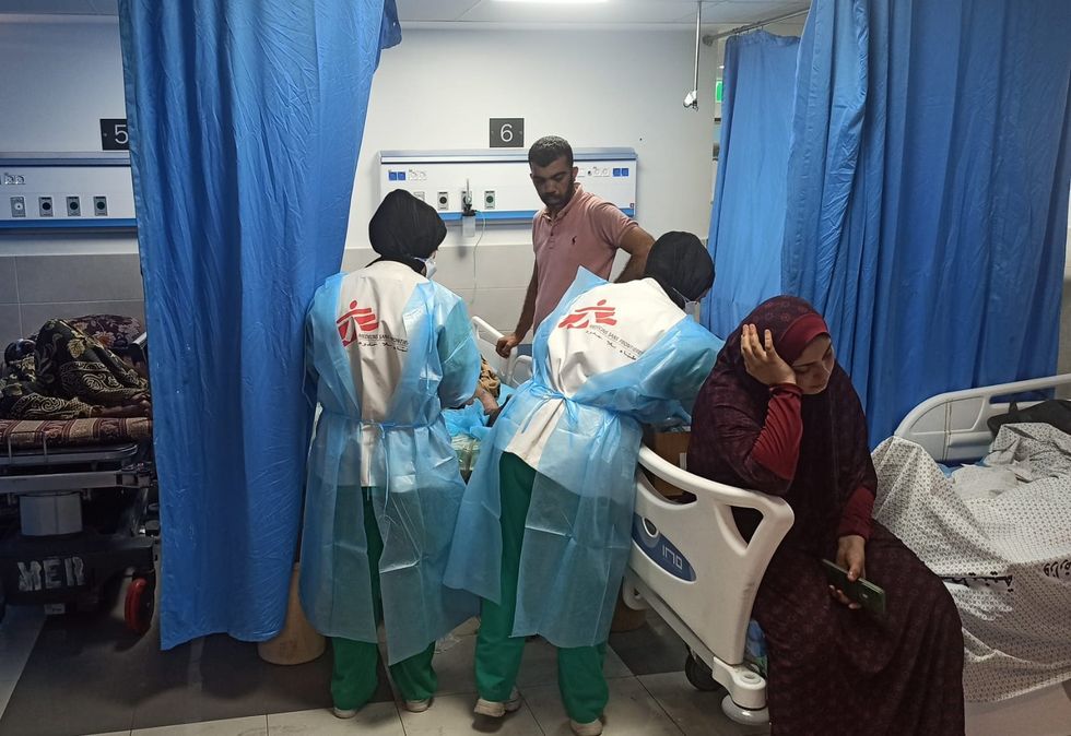 Två medarbetare på al Shifa-sjukhuset i Gaza står böjd över en person som ligger i en sjukhussäng. Bredvid sitter i kvinna på en annan säng.