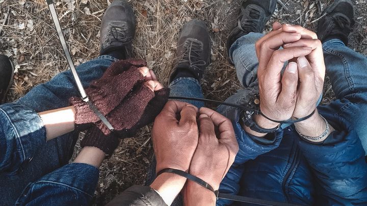 Tre personer på den grekiska ön Lesbos sitter ner på marken, deras handleder är fastspända med buntband.