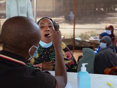 En man använder en träspatel för att undersöka en patient med misstänkt difteri i Nigeria.