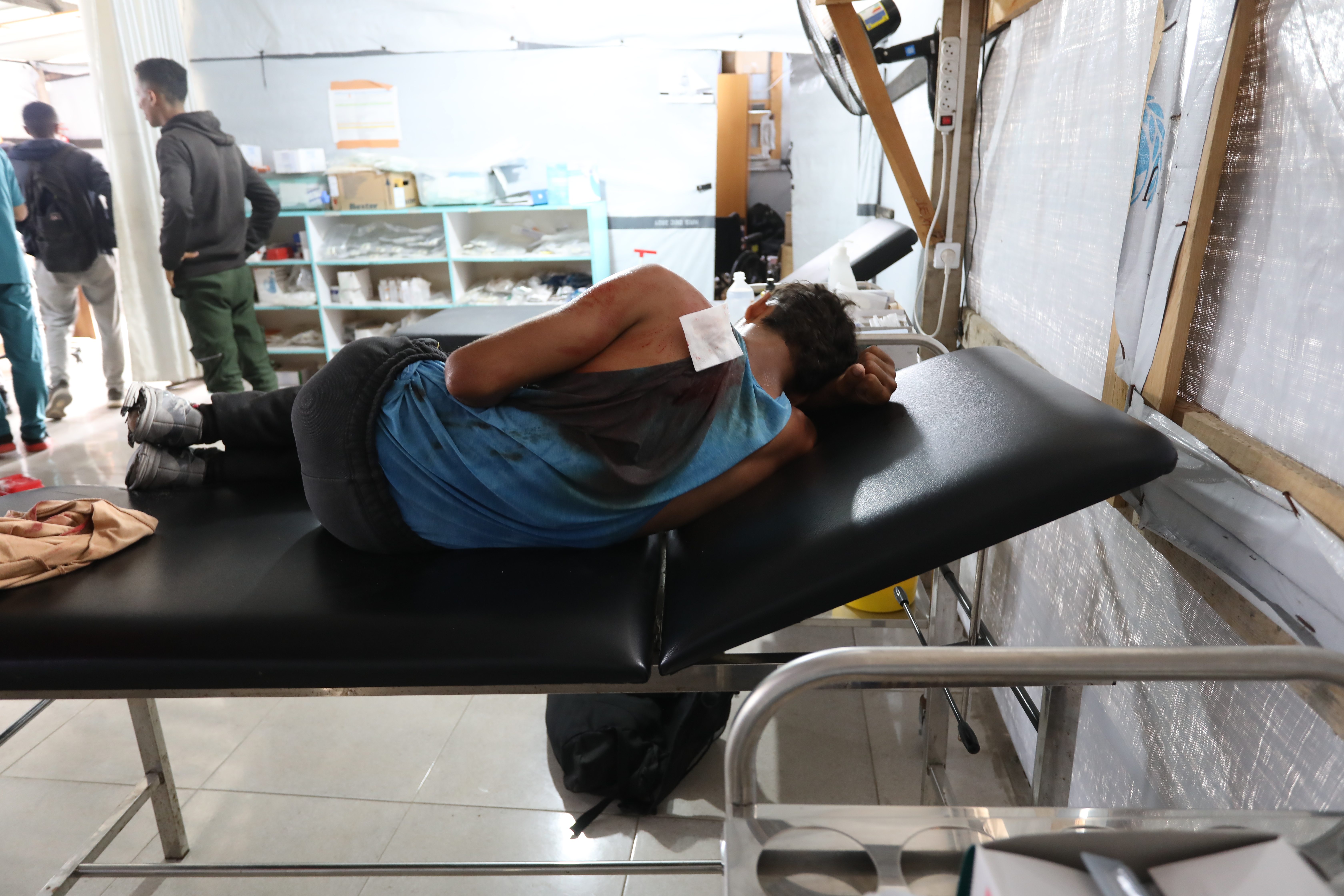 Skottskadade 17-årige Ashraf ligger på en brits på en vårdcentral i Gaza. Hans blå linne är täckt av blod.