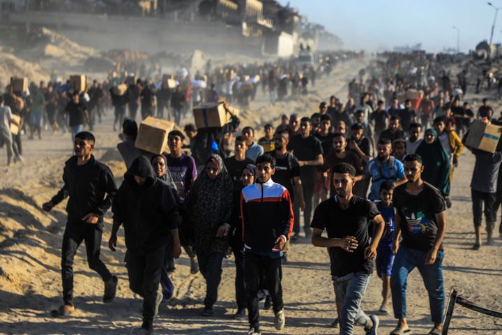 En stor grupp människor går mot kameran på en sandig väg, några bär lådor.