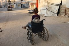 En flicka i rullstol på en gata i Gaza, med skadade byggnader i bakgrunden.