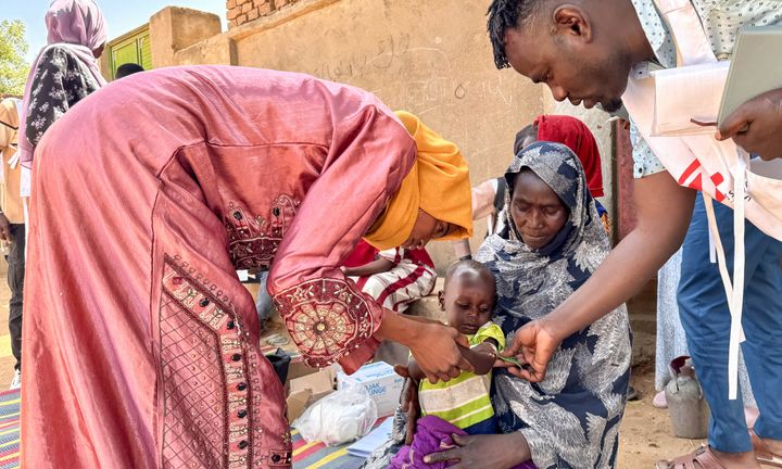 En volontär och en anställd från Läkare Utan Gränser undersöker 18 månader gamla Mohamed Ayoub som sitter i en kvinnas knä.
