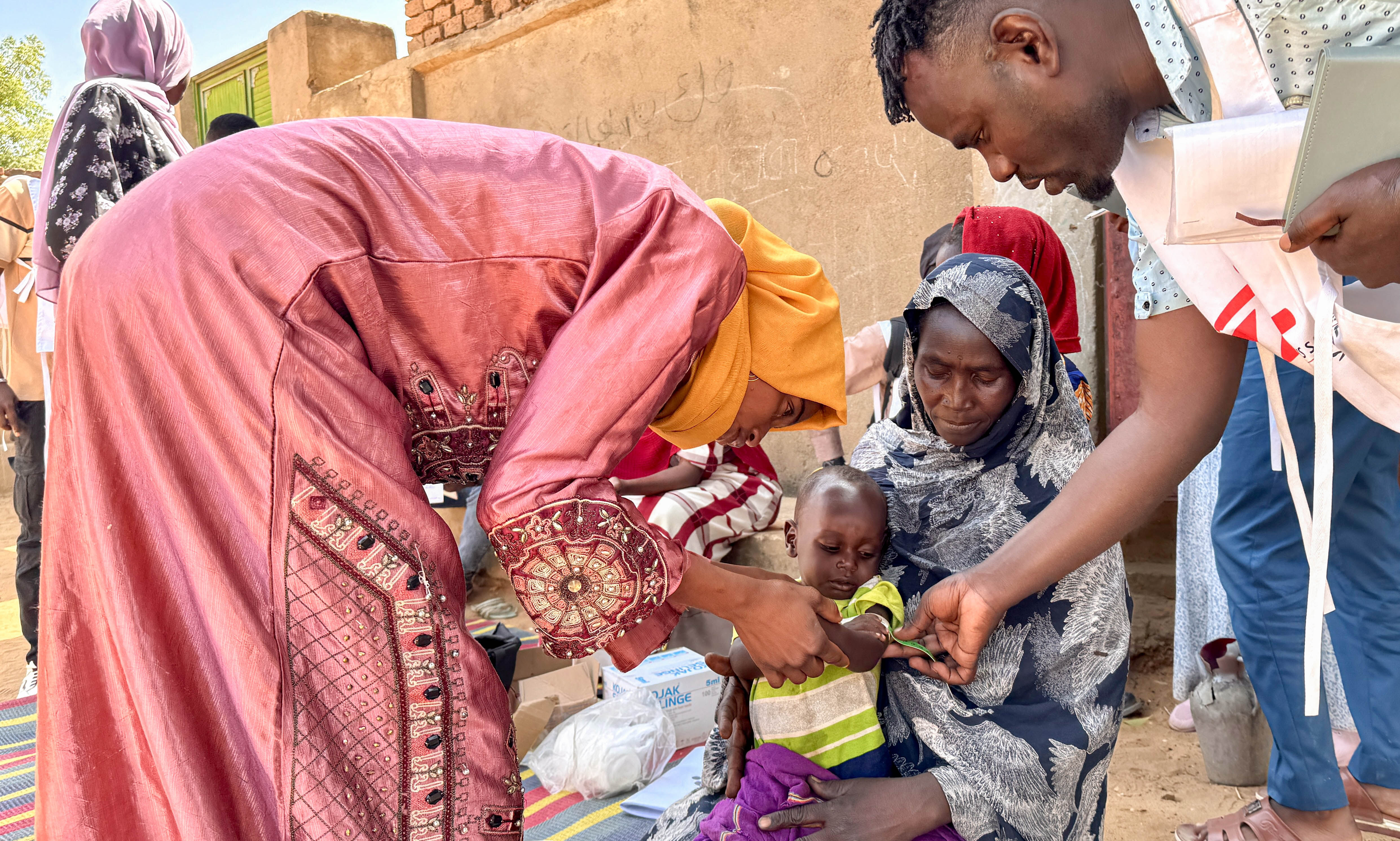 En volontär och en anställd från Läkare Utan Gränser undersöker 18 månader gamla Mohamed Ayoub som sitter i en kvinnas knä.