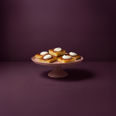 Fem bitar Hälsingeostkaka med klickar av grädde på ett fat.