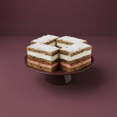 En tårta med flera lager skimrande brun och vit fyllning, dekorerad med florsocker, på ett mörkrött fat mot en lila bakgrund.