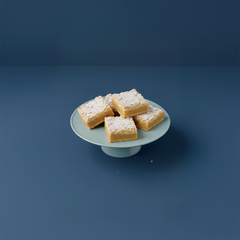 Svenska ölandskakor, fyrkantigt skurna och pudrade med socker, på ett fat mot en blå bakgrund.