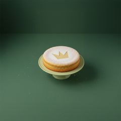 Bild på en rund kaka med en kronformad dekoration av florsocker ovanpå, placerad på ett fat mot en grön bakgrund.