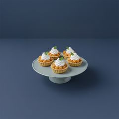 Fyra små körsbärsformade mördegsbakelser toppade med grädde och dekorerade med blad på ett fat.