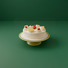 Tårta på ett fat med grädde, dekorerad med fruktbitar och bär, mot en grön bakgrund.