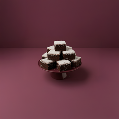 En stapel av chokladrutor med kokos på ett fat mot en mörklila bakgrund.