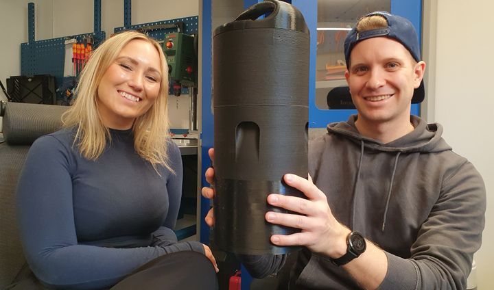 A woman and a man hold a black cylindrical tower 60cm high.