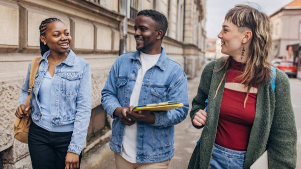 Three multiethnic students share a conversation and smiles while walking on a campus street