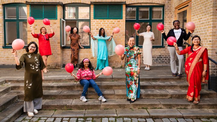 Kvinnor med olika nationaliteter står på trappa och viftar med ballonger.