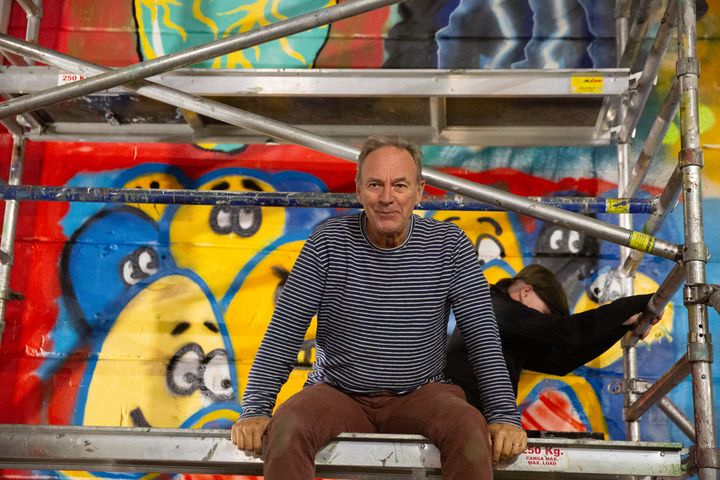 Äldre man sitter på byggställning framför väggmålning.