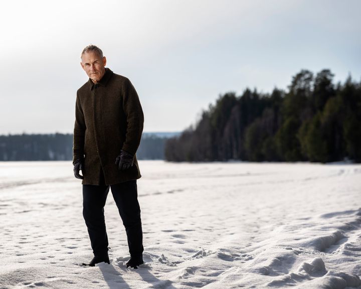 En man står på en snöig mark med skog i bakgrunden.