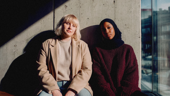 Två personer sitter tillsammans i ett soligt rum, vid en betongvägg. Kampanjbild för Folkuniversitetets yrkeshögskoleutbildningar.