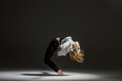 En person dansar med böjd rygg i en mörk studiobelysning.