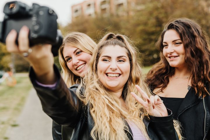 Tre glada personer står utomhus och tar en selfie tillsammans.