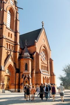 Grupp utanför en stor tegelkyrka i solljus.