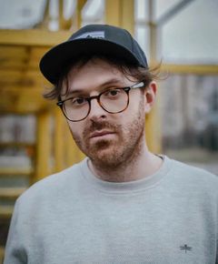 Porträtt på Yll Xhaferi som är en ung man med glasögon och keps på hvuudet.