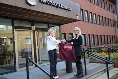 Två ljushåriga kvinnor står framför ett tegelhus och skakar hand