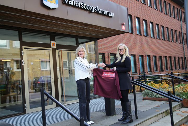 Två ljushåriga kvinnor står framför ett tegelhus och skakar hand