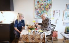 Hemtjänstpersonalen Linnéa Johansson och brukaren Per-Olof Lindell sitter vid ett köksbord.