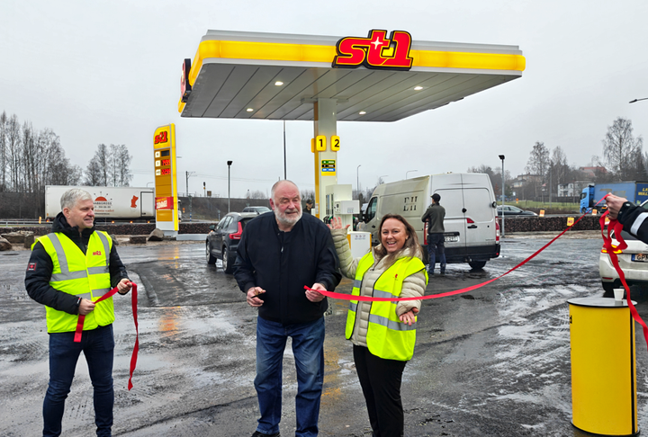 Bandklippning av en man i mörk jacka och jeans framför St1s nya station i Ludvika. En man och en kvinna i gula varselvästar står på varsin sida av mannen i mörk jacka och håller i bandet.