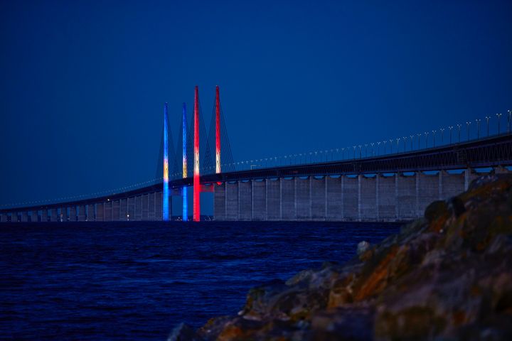 Utsikt över Öresundsbron i skymningen med belysning i Sveriges och Danmarks färger.