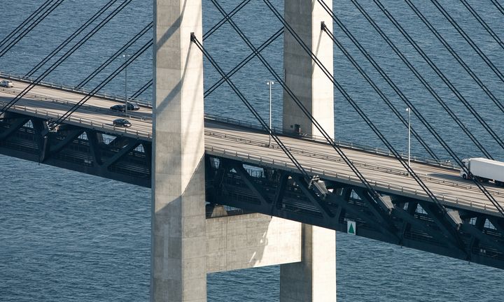 Alt-text: Flygbild av Öresundsbron med bilar och en lastbil som kör över bron, med dess karakteristiska pyloner och kablar synliga mot vattnet.