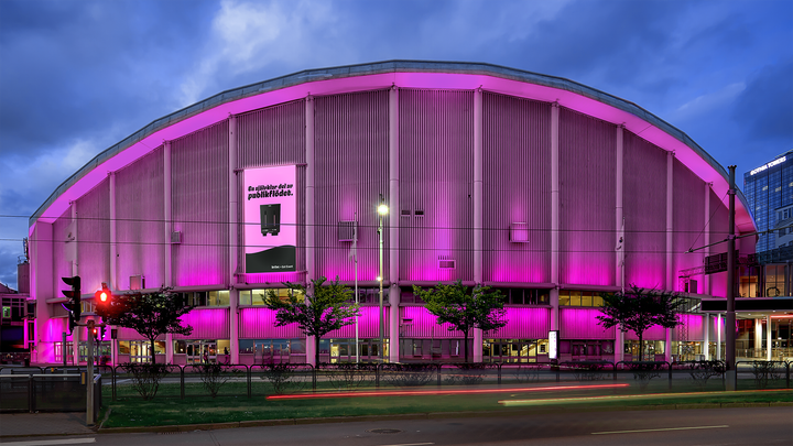 Bild av arenan Scandinavium upplyst i rosa ljus på kvällen.