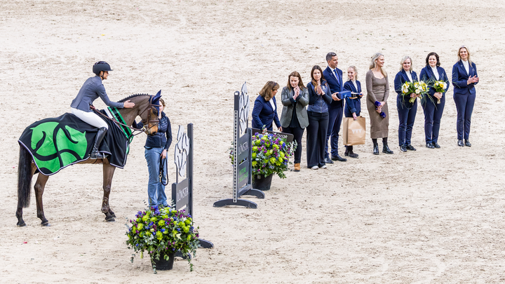 Ryttare på häst tar emot pris bredvid en rad människor med blommor i händerna.